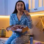 Image of a woman in pajamas snacking at night on pizza