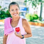Image of a healthy middle aged woman who's just been exercising holding a little red heart.