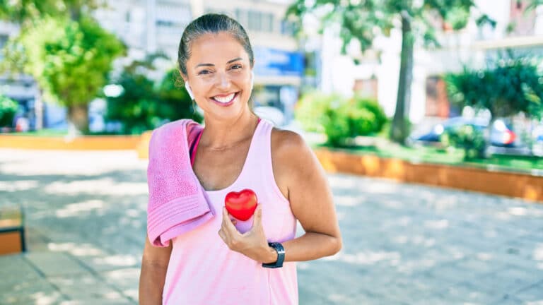 Image of a healthy middle aged woman who's just been exercising holding a little red heart.