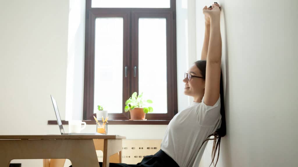 Image of a woman taking a brief break from her work to stretch at her desk and improve posture